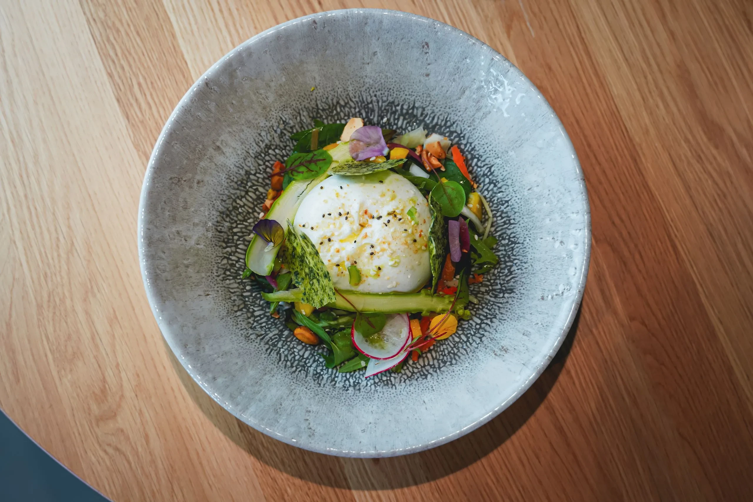 Salade colorée avec burrata sur assiette grise.