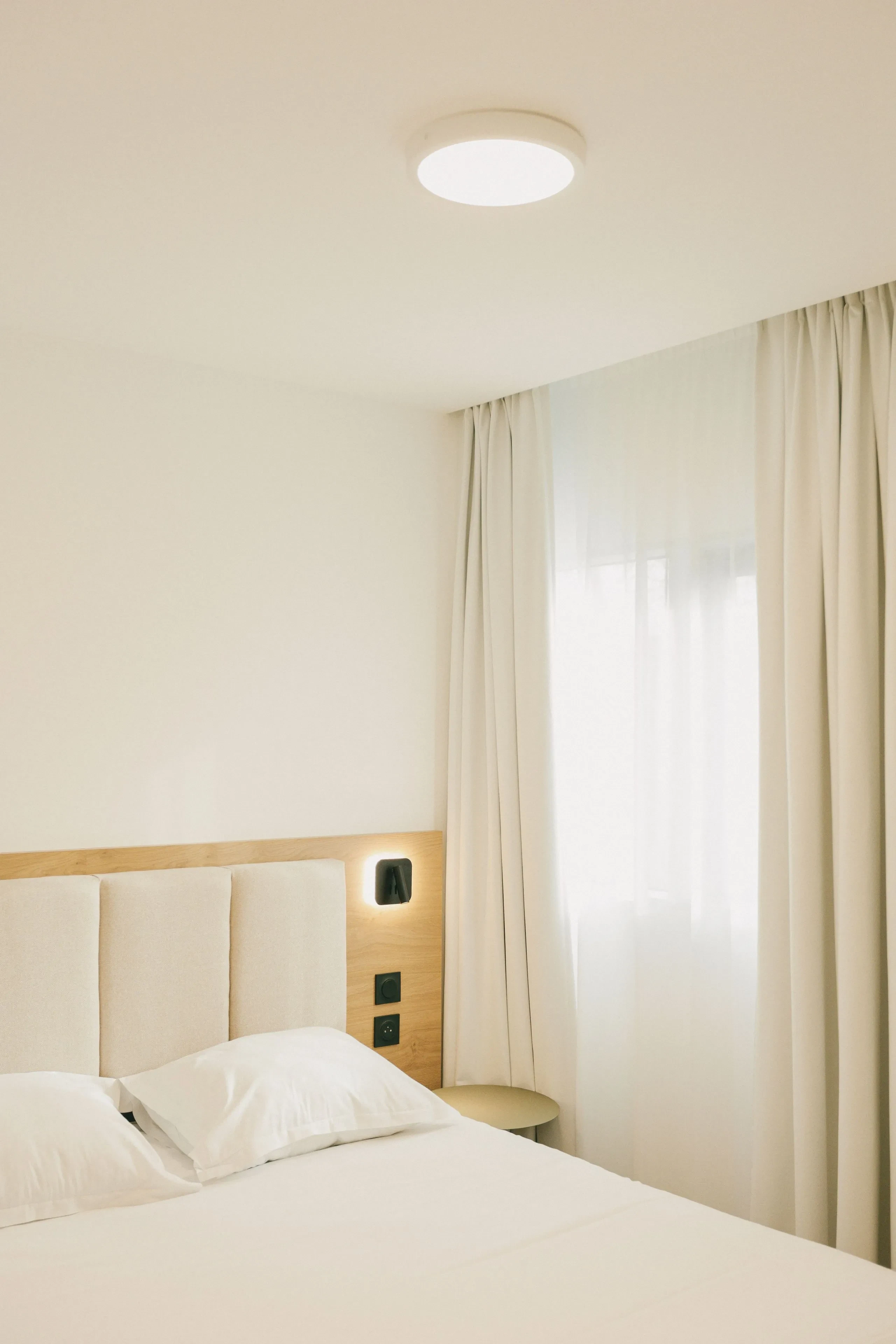 Chambre lumineuse avec lit et rideaux blancs.