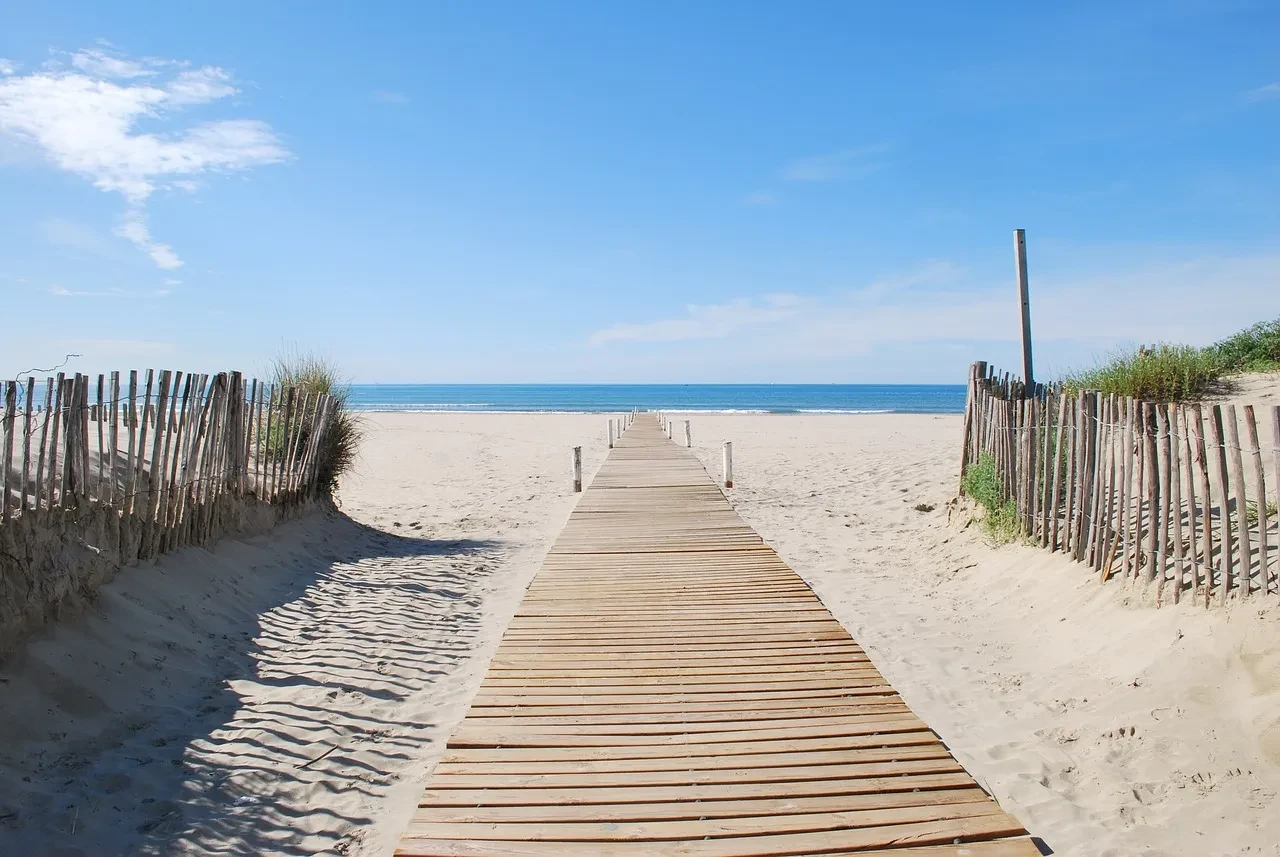 Passerelle en bois sur plage ensoleillée.